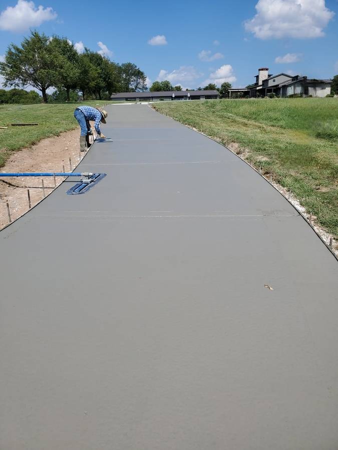 Worker finishing a long concrete driveway at a rural home